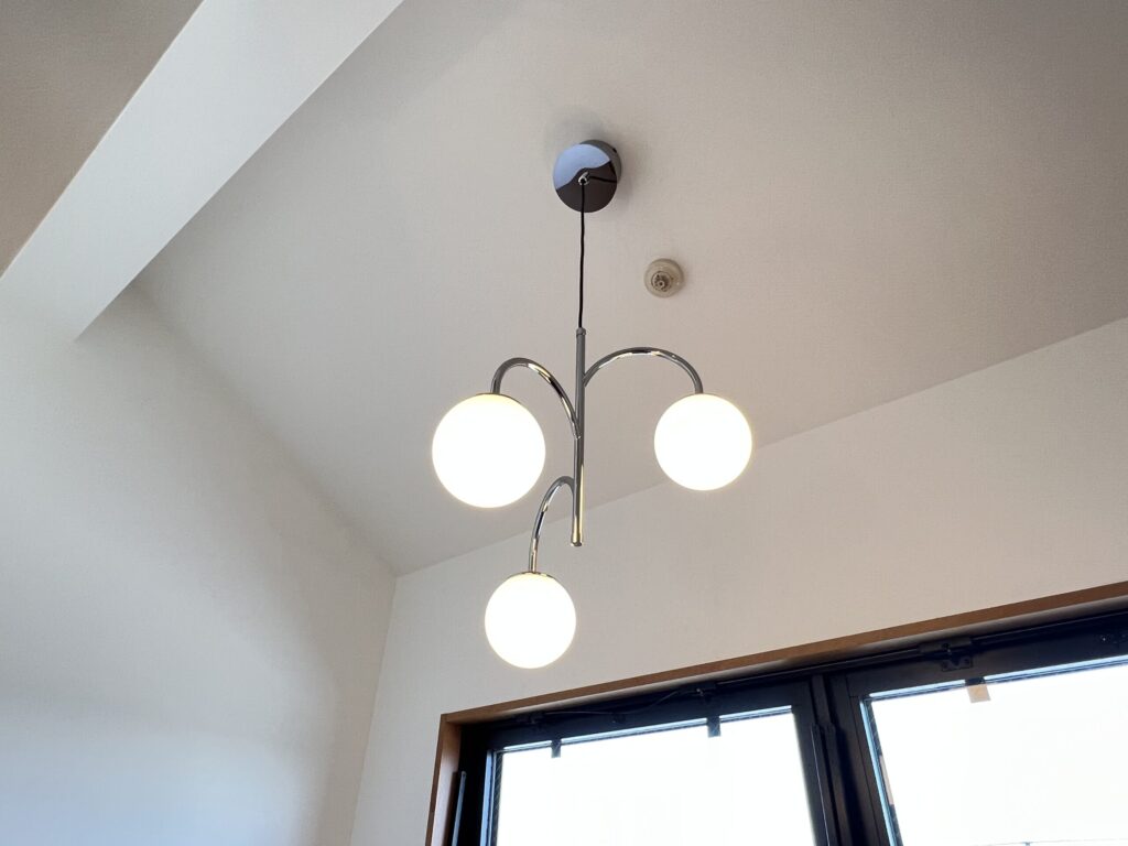 室内装飾の照明交換例。クロームアームに乳白色のガラスボール3灯が付いたデザインペンダントライトを勾配天井に設置している