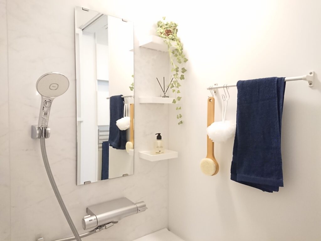 浴室の室内装飾例。ネイビーのタオル・フェイクグリーン・リードディフューザー・ハンドソープ・ボディブラシを配置し、清潔感のある空間を演出している