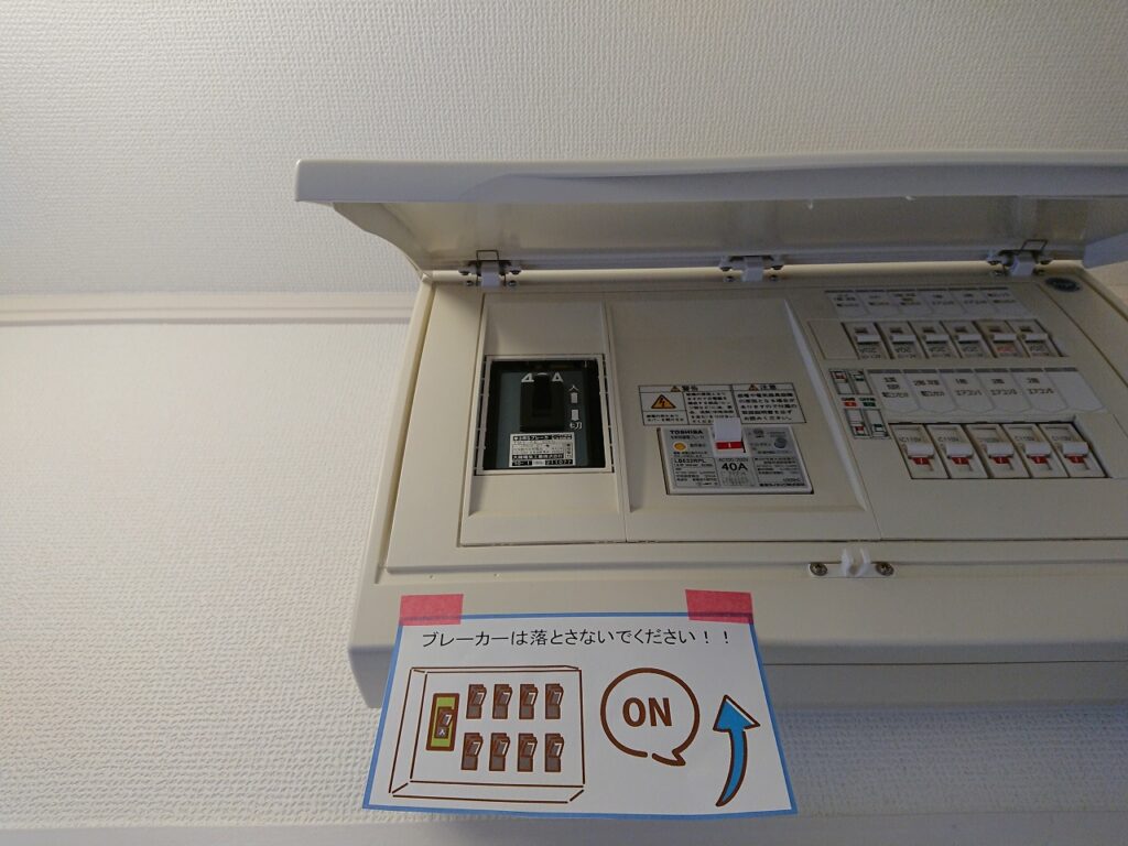 分電盤と注意書きの掲示例。東芝製40Aの分電盤の下に「ブレーカーは落とさないでください！！」と記載したイラスト付きの案内を貼り付けている