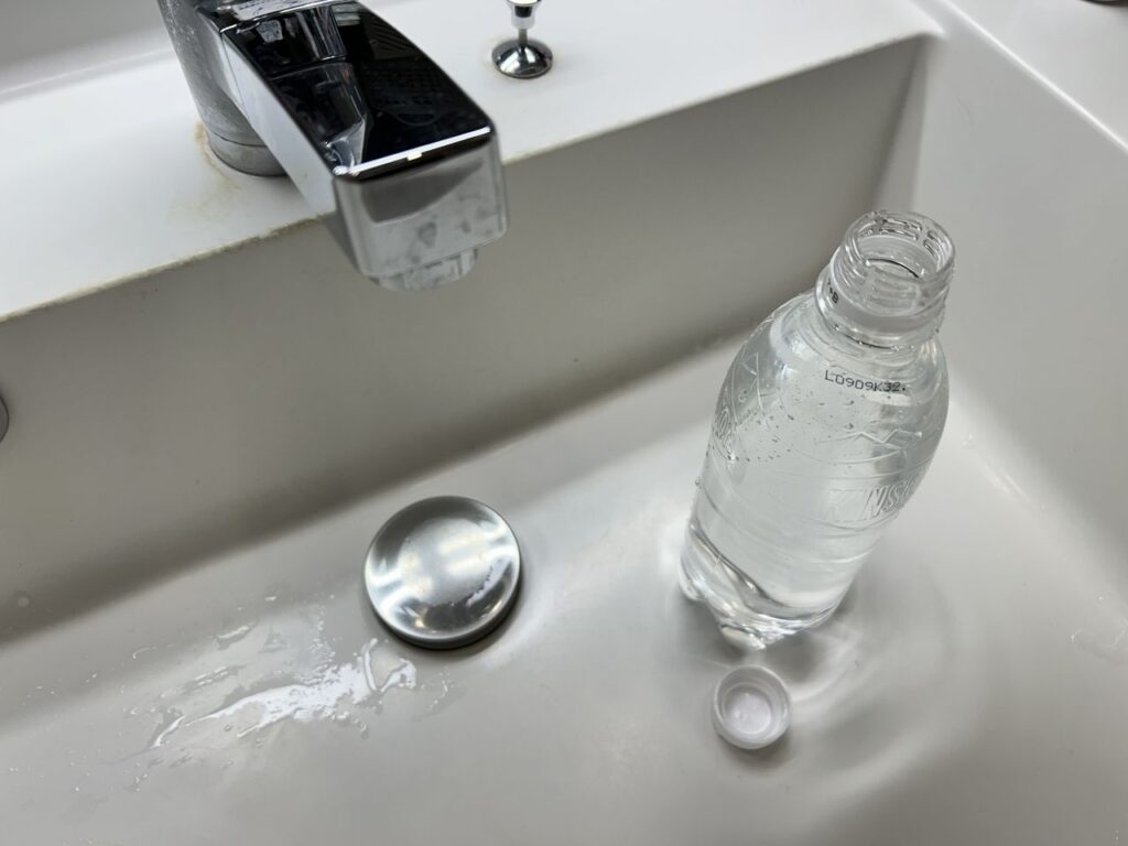 洗面台の排水トラップにペットボトルの水を補給している様子。空き家は水道を使わないため排水トラップの封水が蒸発し、下水の悪臭や虫の侵入原因になる