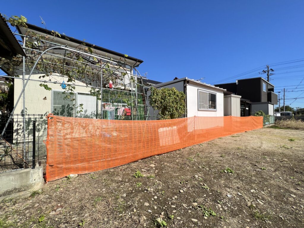 更地へのオレンジネットフェンス設置例。隣地との境界沿いにオレンジ色のメッシュフェンスをペグで固定し、敷地範囲を視覚的に明示している