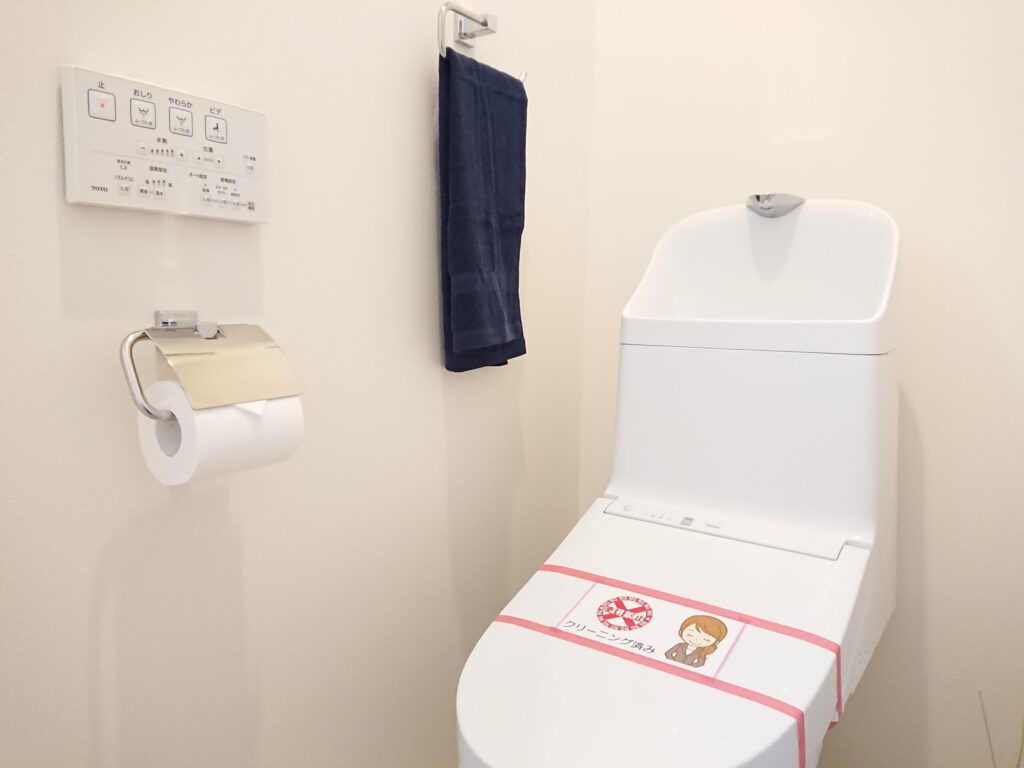 トイレの内覧準備例。TOTO製温水洗浄便座に「クリーニング済み」のシールを貼り、トイレットペーパーとネイビーのタオルをセットして清潔感を演出している